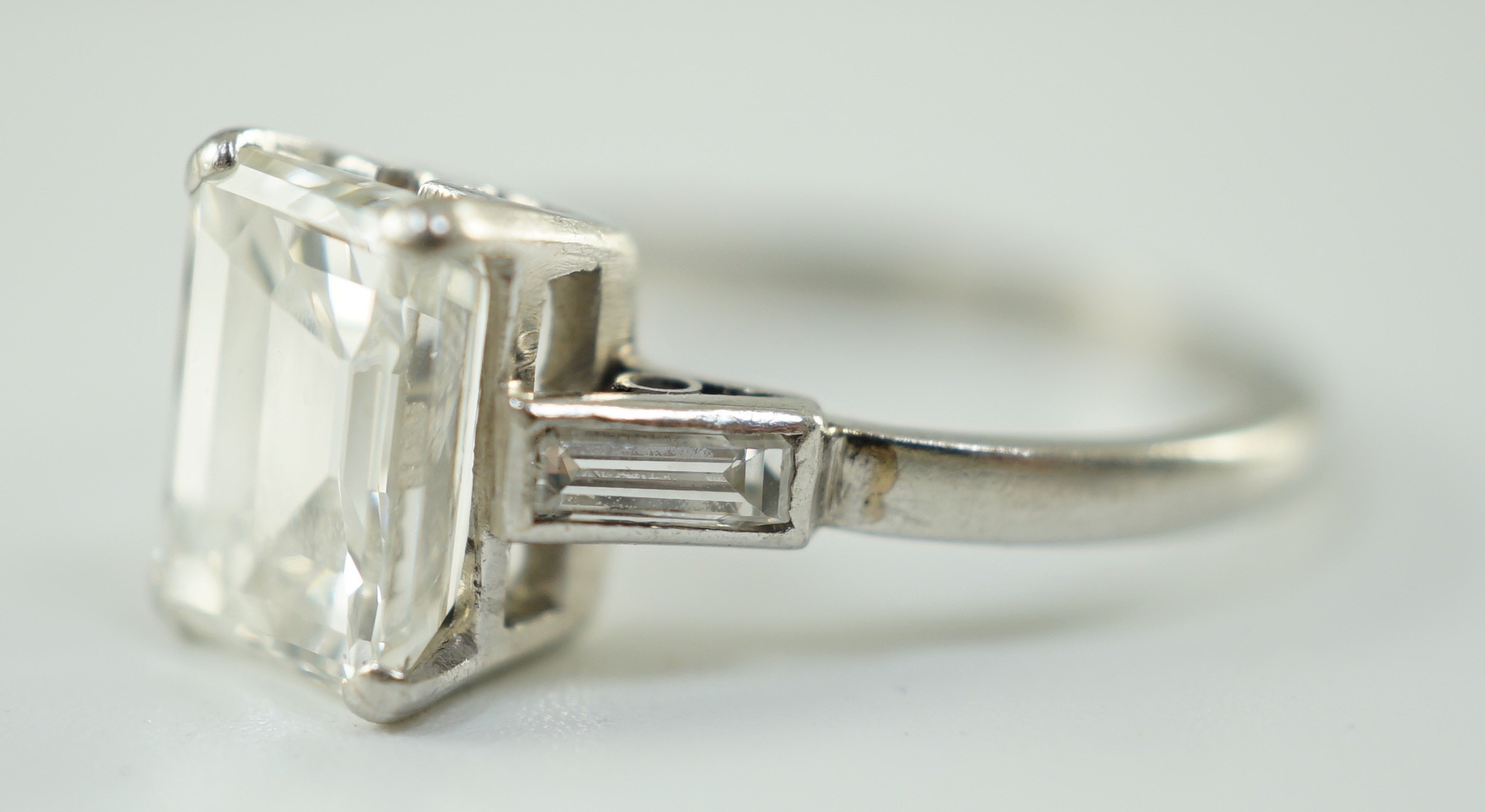 A platinum and single stone emerald cut diamond set ring, with baguette cut diamond set shoulders